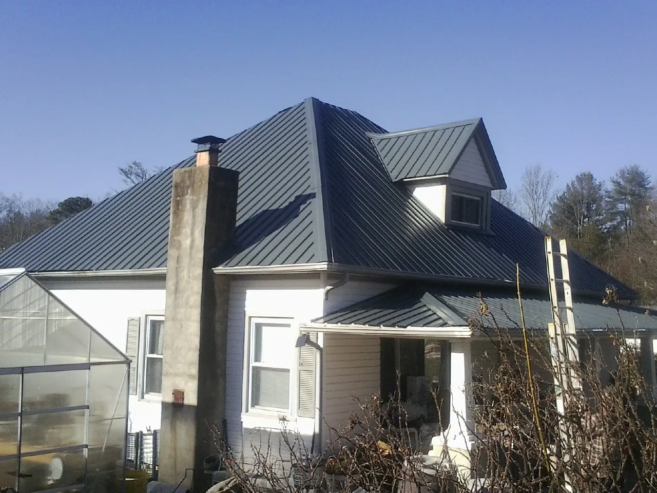 Dark blue standing seam metal roof on a white farmhouse with dormer — Slate & Tile Roof Repair by Roofing Brothers in Monessen