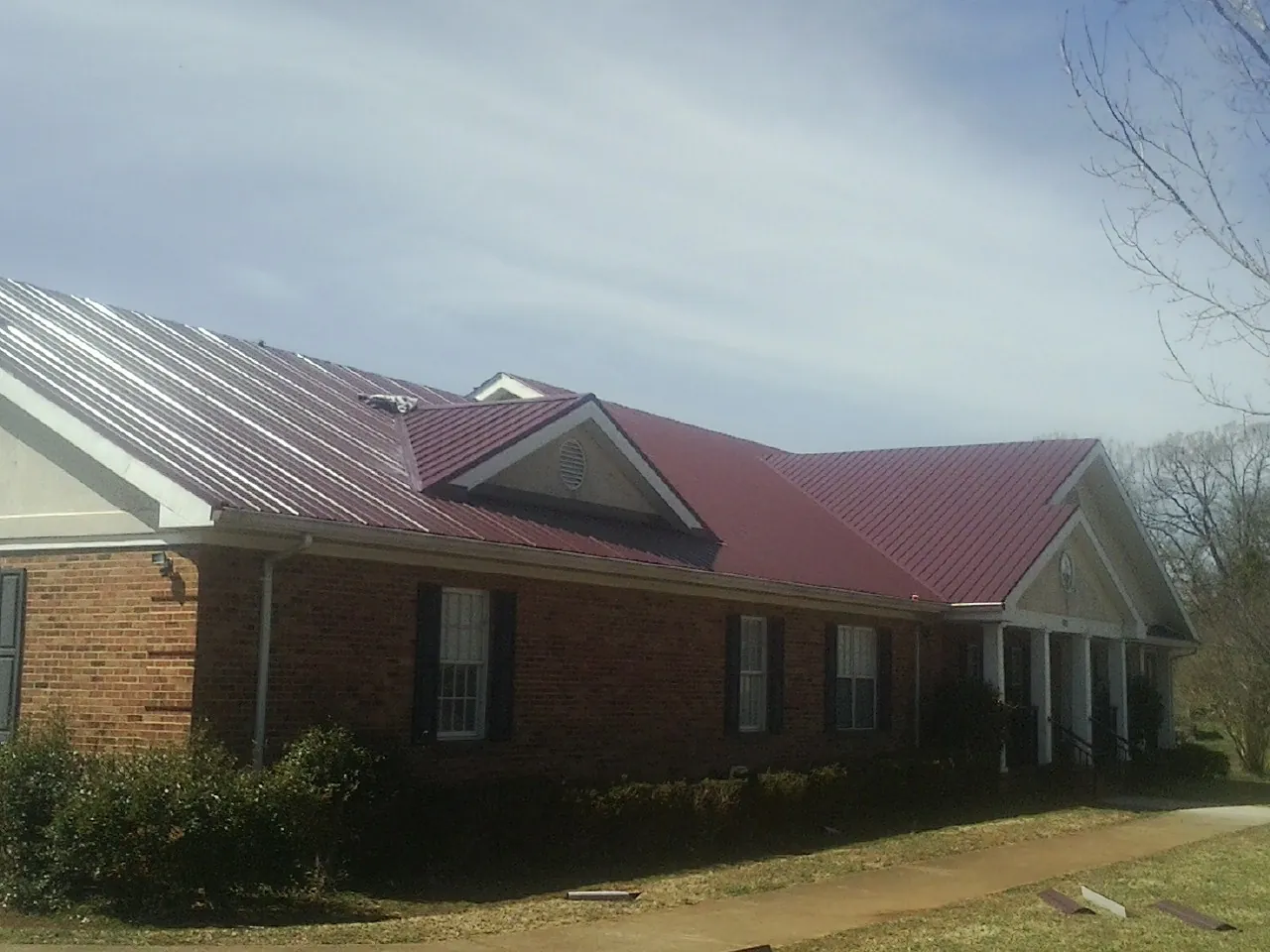 Red metal roof with gabled entries on a long brick building, from a Hail Damage Roof Repair job in Monessen