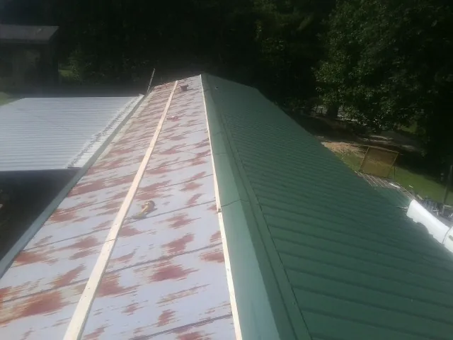 Old rusted panels beside newly installed green metal roofing — Wind Damage Roof Repair by Roofing Brothers in Monessen