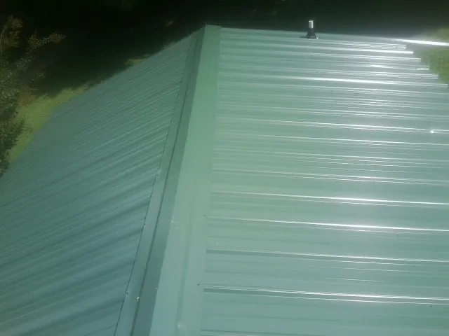 New green metal panels meeting at the ridge of a roof — Flat Roof Repair work by our crew in Monessen