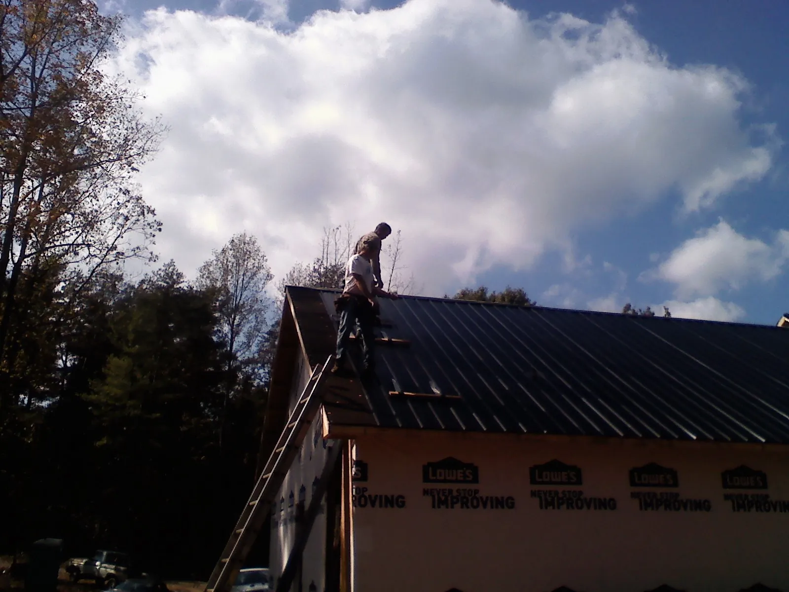 Roofer fastening dark metal panels high against a cloudy sky, from a Roof Inspection job in Monessen