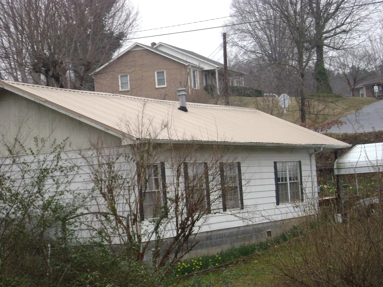 Tan metal roof on a white sided house set into a hillside — Commercial Roofing by Roofing Brothers in Monessen